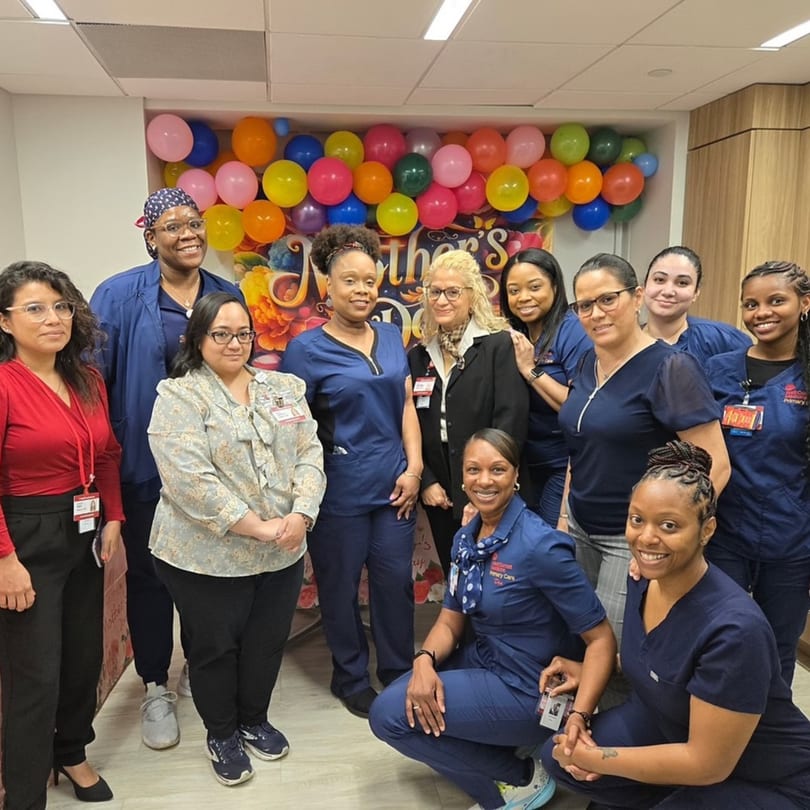 A group of women, some in scrubs, posing in front of a colorful balloon display.