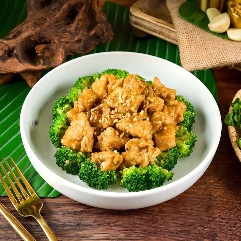 Thai chicken with peanut sauce and broccoli florets in a white bowl on a wooden table.